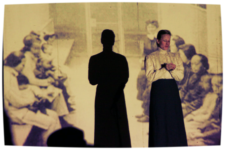 Andrea Day as the missionary, Miss Gregory, in front of archival image of detained Chinese women on Angel Island.