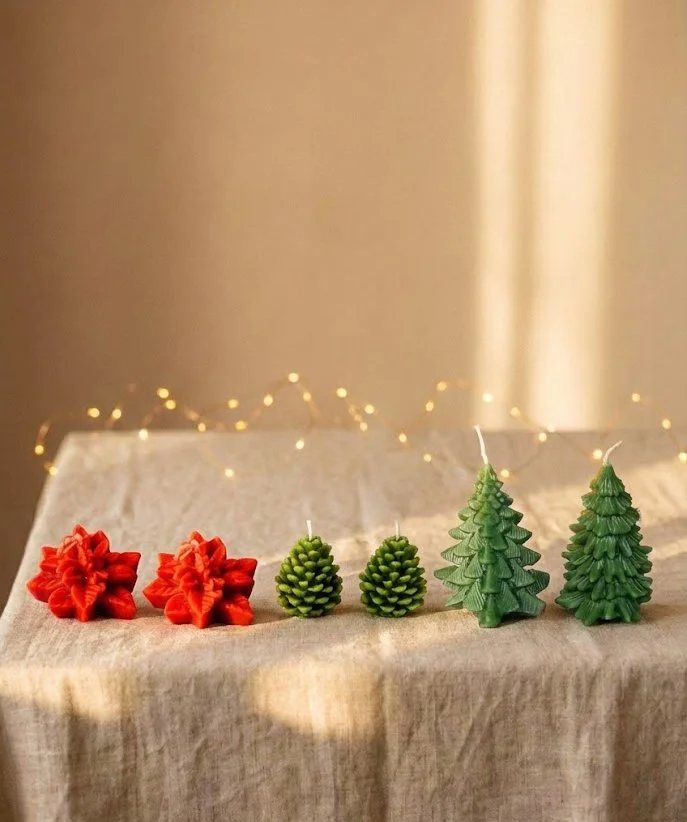 Small 7x5 gift box containing two green sculpted beeswax Christmas trees, two red poinsettias, and tiny green beeswax pinecones.