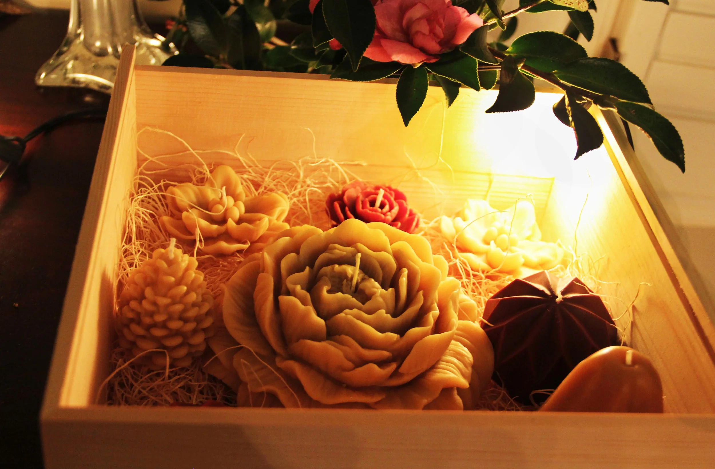 Large 10x10 gift box featuring sculpted beeswax camellias and a large peony, styled in a winter garden setting with garnet ornaments and natural pinecones.