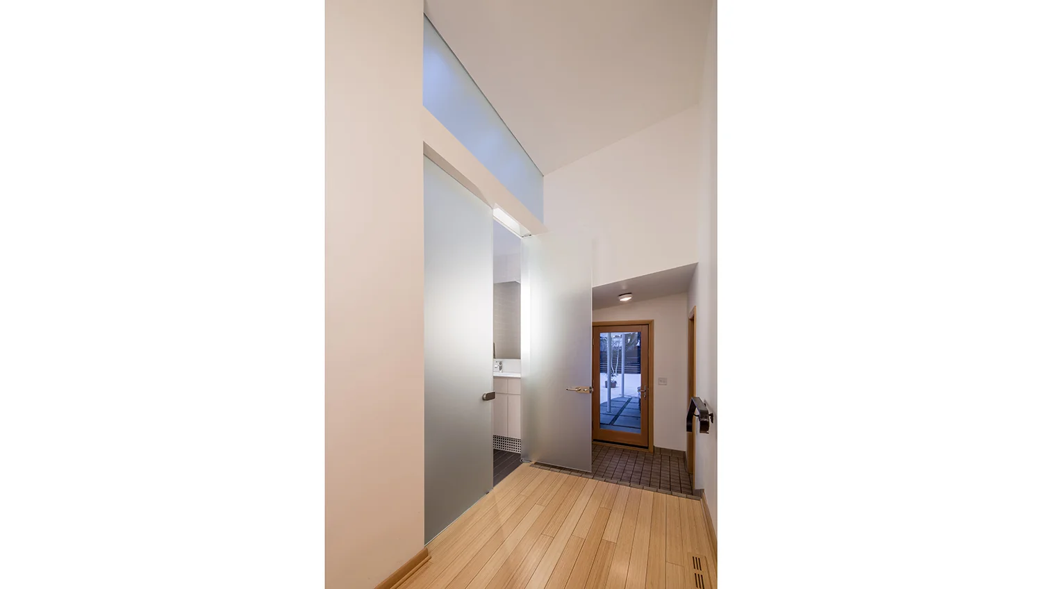 MID-CENTURY REMODEL This design is the final and unifying renovation in a series of updates to a dated mid-century home along the Mississippi River in Minneapolis. The project features a flexible multi-purpose basement family room, a new floating stair visually connecting the formerly isolated and dark basement to the main floor living space, three updated bathrooms, and a new mudroom / laundry room. Expanding upon the material palette and design language of a very refined and modern kitchen renovation and exterior update (completed previously by a different architect and landscape designer and featured in Better Homes and Gardens and Midwest Home), this final phase of work emphasizes brightening the interior space and the use of natural daylight throughout. Strategies include the use of increased window opening sizes, translucent glass walls, and skylights to allow natural light deeper into formerly dark interior spaces. The material palette features light colored bamboo floors and Baltic birch paneling (to match the existing Scandinavian blonde woodwork) as well as highly reflective glossy material selections for the bathroom wall tile, cabinetry, and powder coated steel stair structure. This renovation project builds on the homeowners adventurous, elegant, modern design sensibility with the use of translucent glass bathroom walls and doors, which transform bathrooms into light transmitting filters between the home exterior and formerly dark interior spaces. The refined and subtle design sensibility of previous renovations is carried forward with a quiet, neutral palette that emphasizes lightness, reflectivity, and textural variation. Photographer: Brandon Stengel www.farmkidstudios.com Project Team: Bob Ganser AIA, Principal-In-Charge Ben Awes AIA Christian Dean AIA