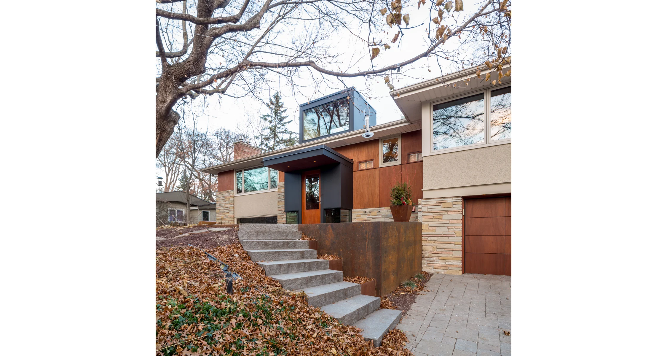 NEW LIFE AT THE SPLIT-LEVEL
Built in the mid 60’s, this wonderful split level home had been updated over the years. Unusual to this era of home, the kitchen, living, and dining are in an area 40’ long by 16’ wide, creating an experience of being close to the outdoors. The one space that was never updated was the entry. Small and cramped, it was the only place in the house that was on “ground level”, yet also the most disconnected from the outside. Three elements were identified and distilled to respond to this condition, connecting the house to the ground through the entry experience. The floor plane: Here we built a new raised front patio and paved the surface, including the entry landing, and the treads and risers, with a course bluestone ceramic paver. The continuation of this surface, flowing inside and out, highlights the “split” in the home as the place of connection to the outside. The wrapper: We struck two lines marking this in-between zone of the landing; a strong existing window line of the basement level, and the new ceiling plane of the entry aligned with the top of the new interior railing. Below this zone is glass, drawing your attention to the ground, allowing the floor to visually move inside and out. Above, a wood surface wraps the interior and defines the entry. The pattern, laser etched into the wood, references the ashlar of the existing stone and transforms from wall to screen as it moves around the space. The sky: The old entry was short, dim, and confined. The new entry rises up and brings light over the full entry stairwell, filling the center of the house. The front monumental window is always dappled by the mature oak that anchors the site. Photographer: Brandon Stengel www.farmkidstudios.com Location: St. Louis Park, MN Completed: 2013 Project Team: Ben Awes AIA, Principal-In-Charge Bob Ganser AIA Christian Dean AIA Nate Dodge