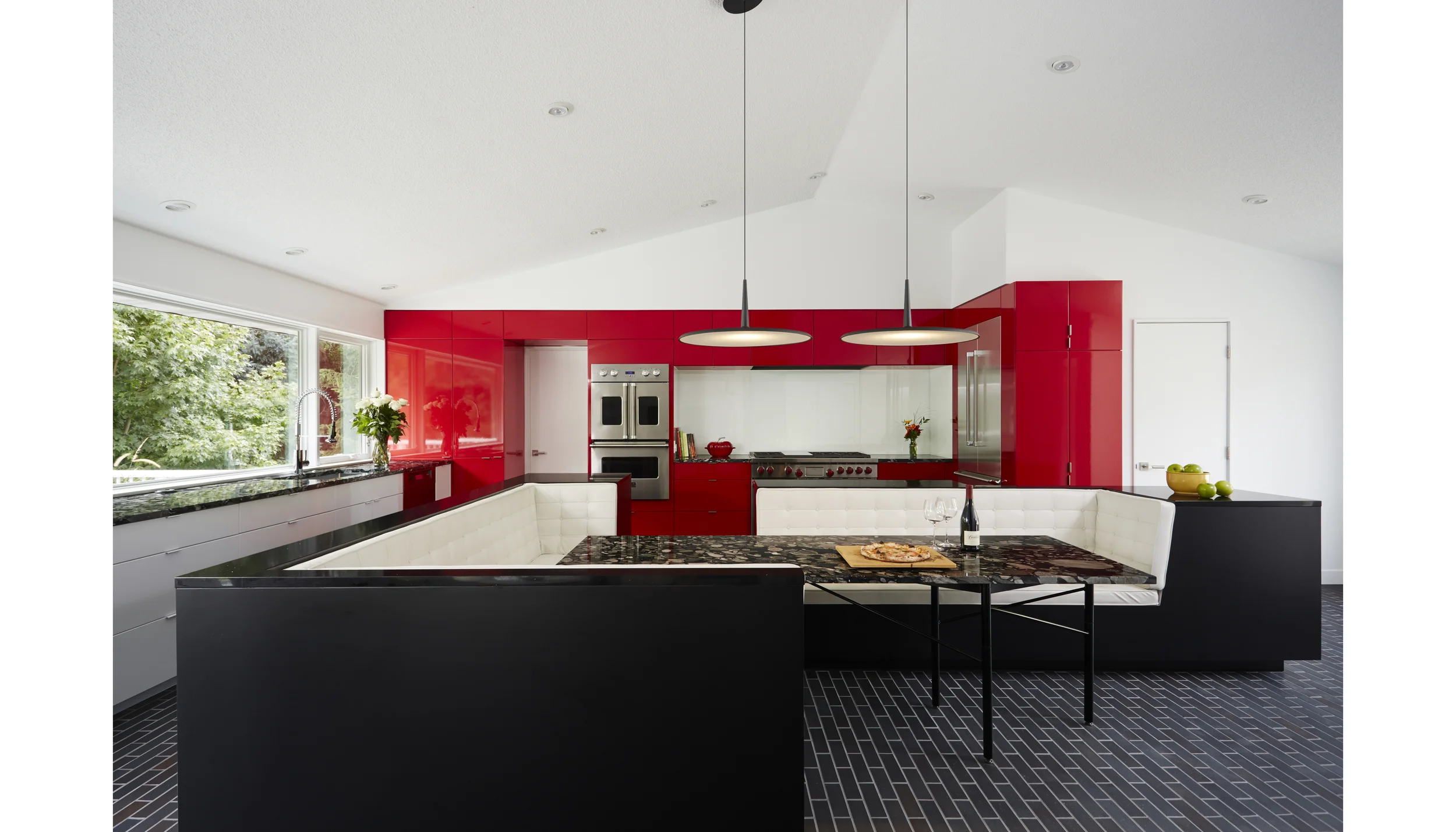 The Gathering Kitchen - re-placing eating at the center of the home. We’ve all had the common experience of guests gathering in the kitchen. It seems the kitchen has replaced the hearth as the center of the modern home. Often in this shift is the loss of gathering around the table. This client has a passion for cooking and has lived for 20 years with a kitchen that’s fallen short of her needs, and a dining room that is never used. She also has a passion for hosting her family & friends – large groups, lively and animated! We combined the space of both rooms to make one large gathering kitchen. The centerpiece is the island which was split open and pulled apart to make place again for gathering around the meal. The island provides functioning countertops and ample storage, as well as enclosure for the full dining table. An adjustable 6-legged table base, as well as unique Marinace granite, cherry red cabinets, and Manganese Ironspot brick highlight the material palate. Photographer: Alyssa Lee www.alyssaleephotography.com Project Team: Ben Awes AIA, Principal-In-Charge Bob Ganser AIA Nate Dodge