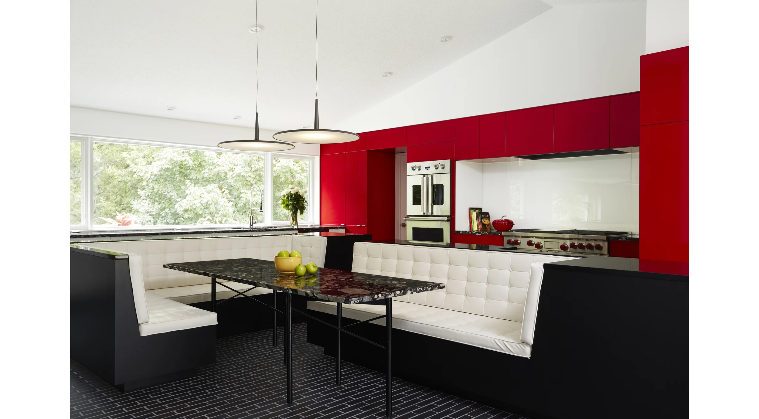The Gathering Kitchen - re-placing eating at the center of the home. We’ve all had the common experience of guests gathering in the kitchen. It seems the kitchen has replaced the hearth as the center of the modern home. Often in this shift is the loss of gathering around the table. This client has a passion for cooking and has lived for 20 years with a kitchen that’s fallen short of her needs, and a dining room that is never used. She also has a passion for hosting her family & friends – large groups, lively and animated! We combined the space of both rooms to make one large gathering kitchen. The centerpiece is the island which was split open and pulled apart to make place again for gathering around the meal. The island provides functioning countertops and ample storage, as well as enclosure for the full dining table. An adjustable 6-legged table base, as well as unique Marinace granite, cherry red cabinets, and Manganese Ironspot brick highlight the material palate. Photographer: Alyssa Lee www.alyssaleephotography.com Project Team: Ben Awes AIA, Principal-In-Charge Bob Ganser AIA Nate Dodge