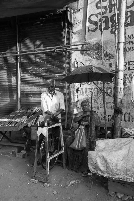 Madame waits under the parasol as her knives are sharpened