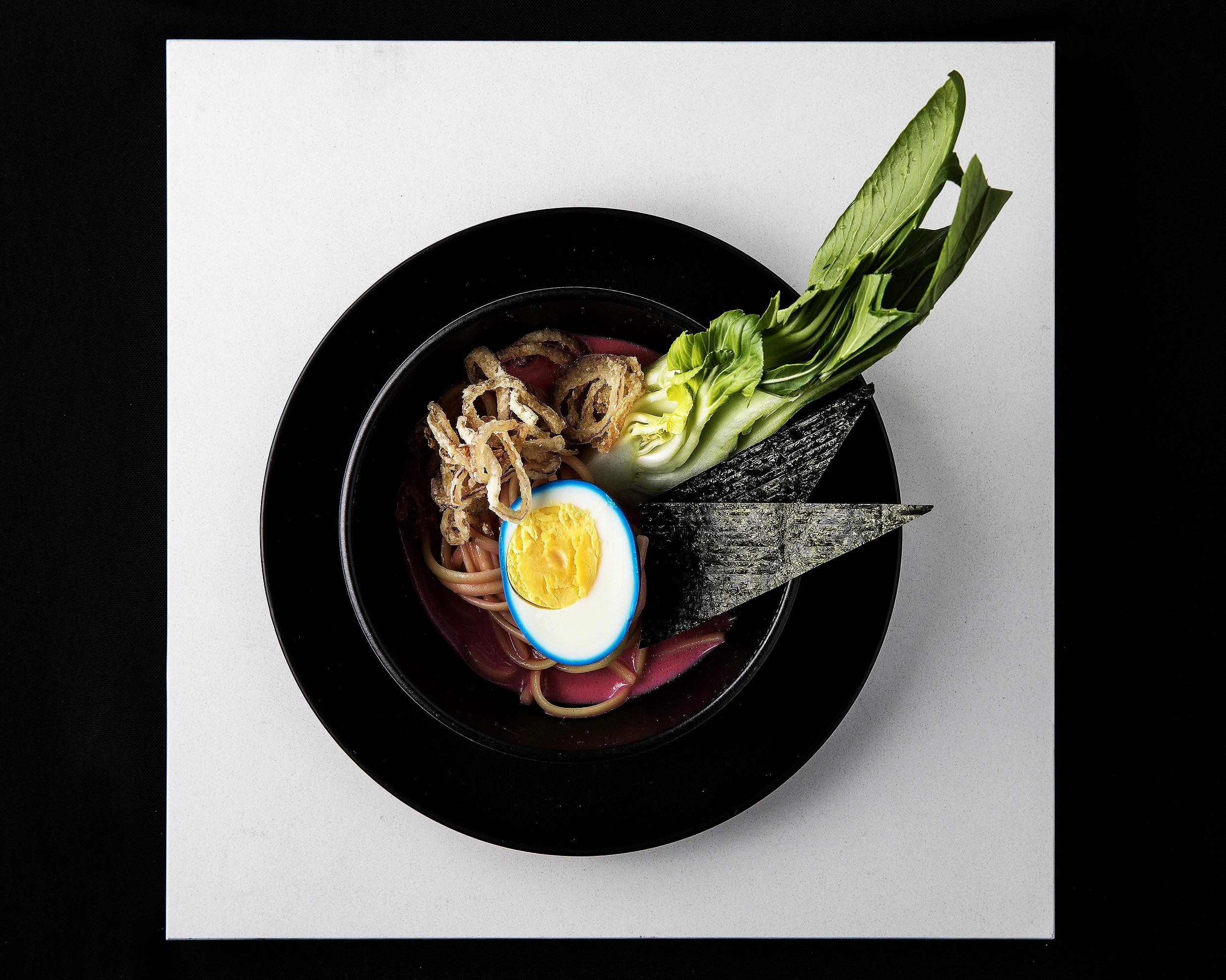 Ramen with pink broth, blue soft boiled egg and crispy onion
