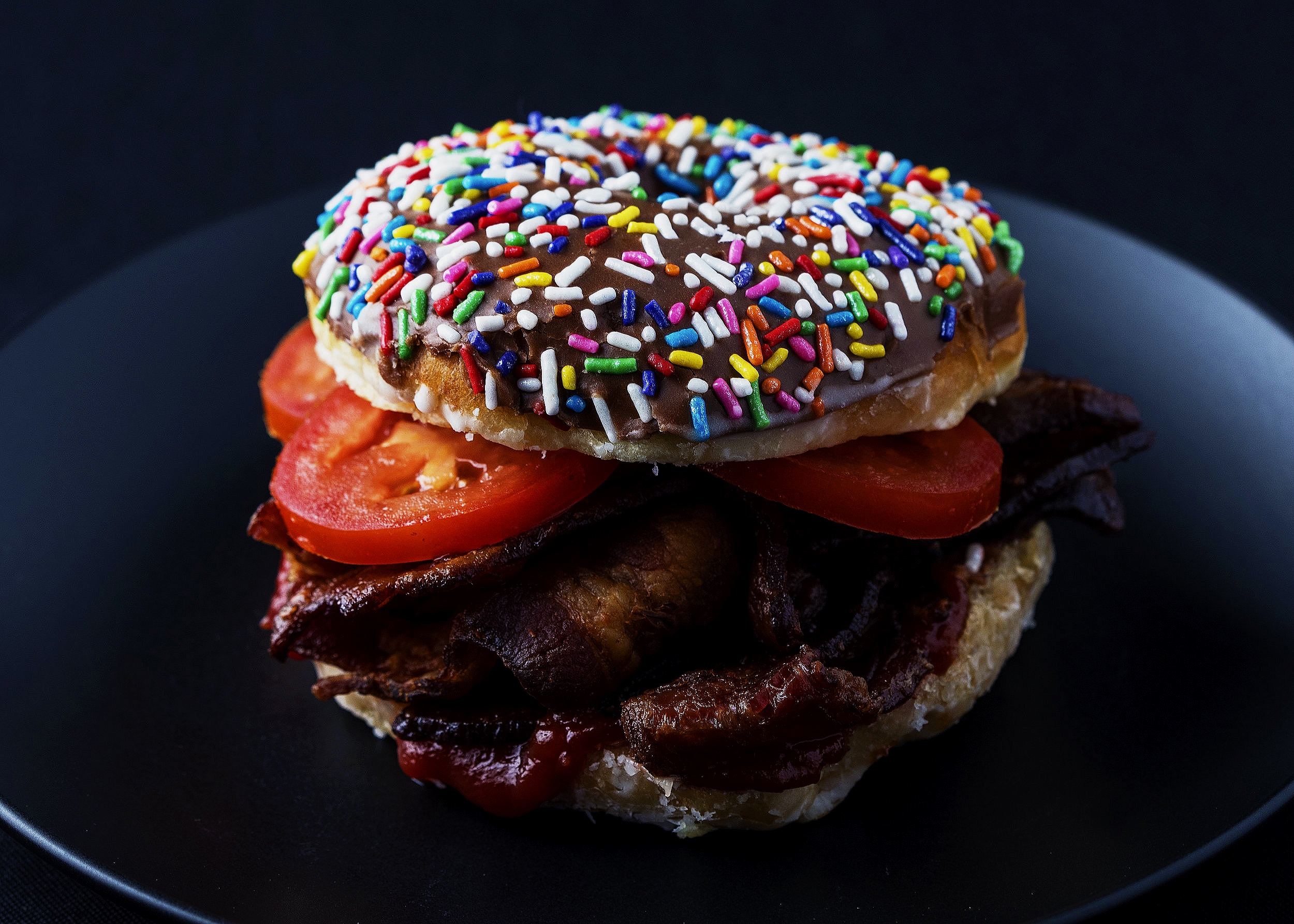 Bacon donut with tomato and ketchup on chocolate sprinkle donut