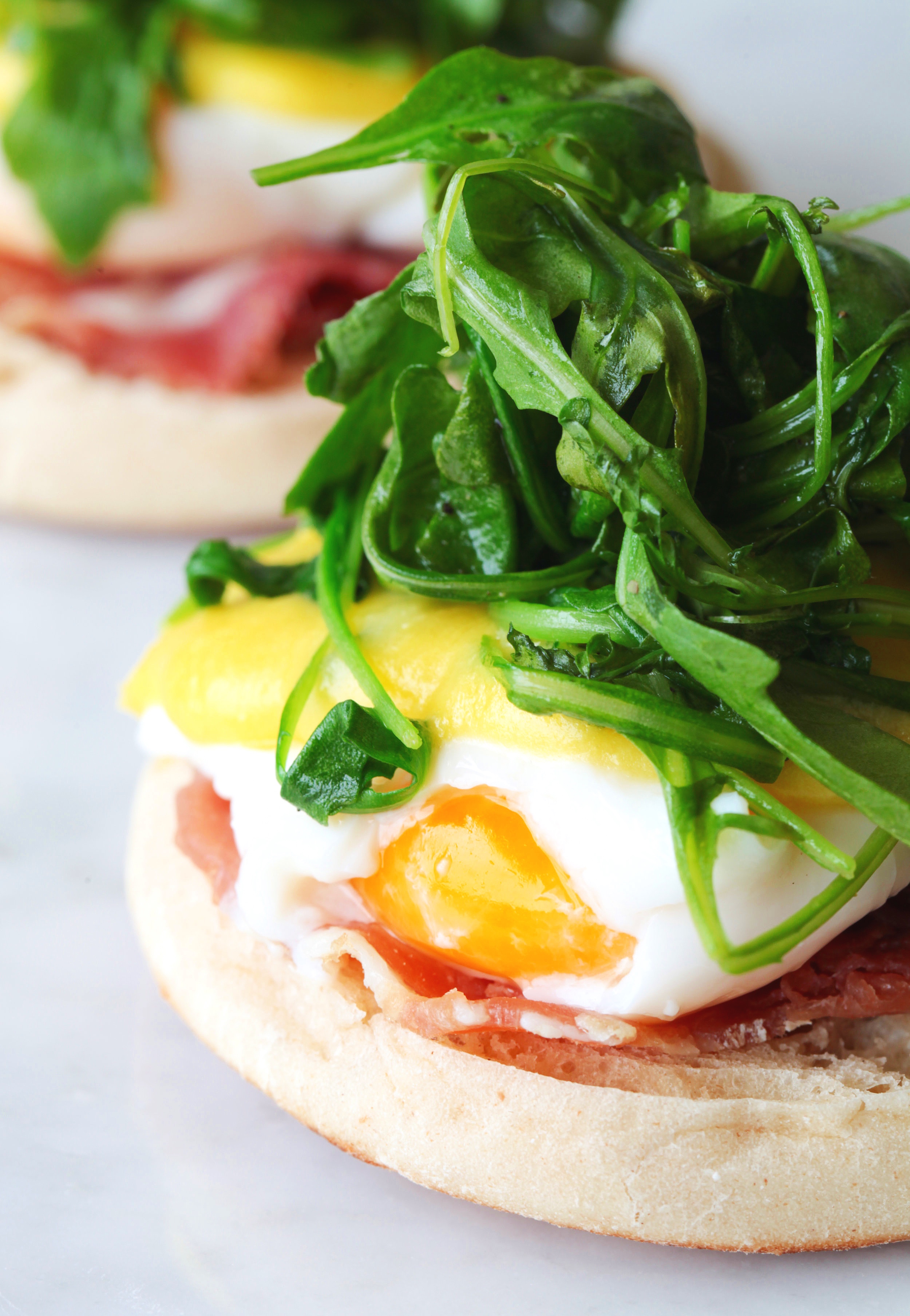 Breakfast sandwich with prosciutto, arugula and sunny side up egg on English muffin