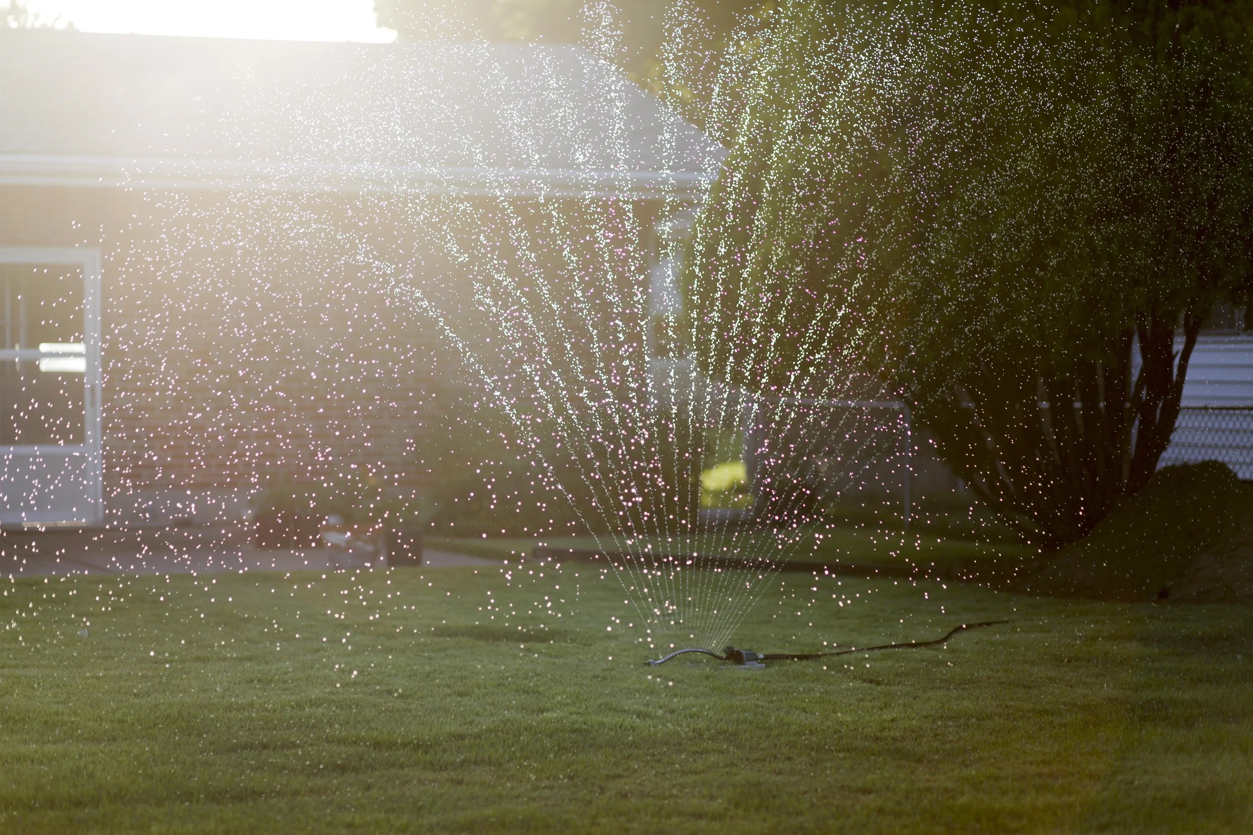 A sprinkler waters a backyard lawn that abuts W. Florissant Ave., where protests have taken place nightly August 20, 2014 in Ferguson, MO.
