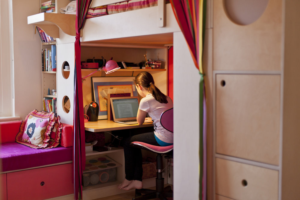 Child studying at a desk under a loft bed in a cozy room.