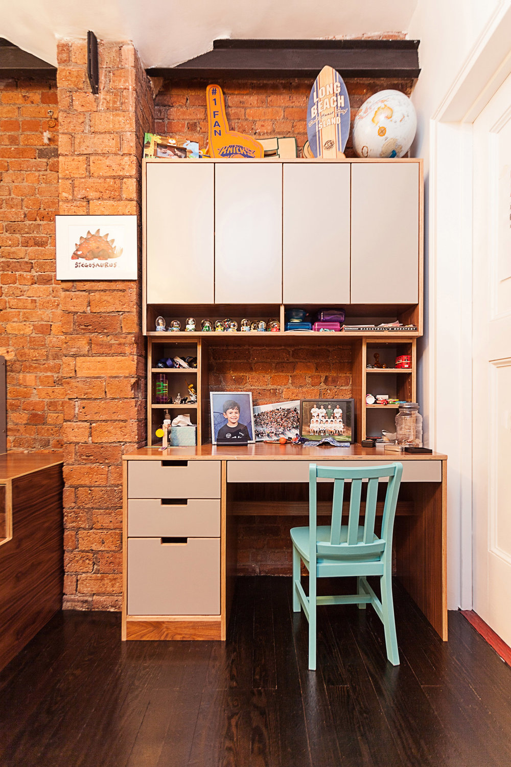 Cozy home office with wooden desk, blue chair, shelves, and a brick wall backdrop.