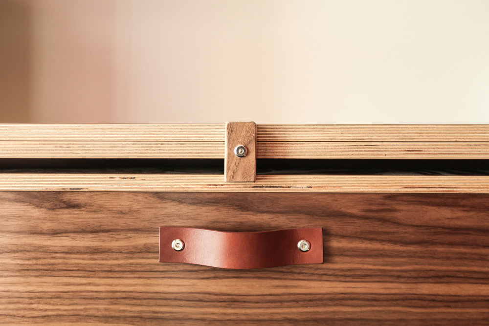 Close-up of a dark wooden drawer with a stylish leather pull handle, showcasing fine craftsmanship.