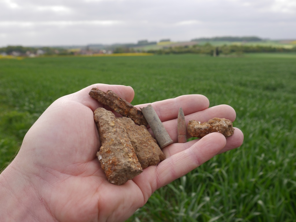 Battlefield debris picked up from no-man's land, just outside the British front line looking towards Fricourt New Cemetery (above my forefinger), with the Tamour mines area in the wood beyond, the Bois Francais on the far ridge beyond that and the village of Fricourt to the left. The shell fragments are likely to be from the German barrage that opened up on no-man's land during the morning of 1 July, adding to the carnage among wounded men who had been hit by machine gun fire during the initial assault. The broken British .303 cartridge (easily distinguished from German cartridges by its rimmed base) and the German 7.92 bullet, found where I am standing, are particularly poignant finds - the machine gun in Fricourt would have been aimed to hit men at waist height as they were advancing down the slope, with spent bullets ploughing into the ground about where I am standing.