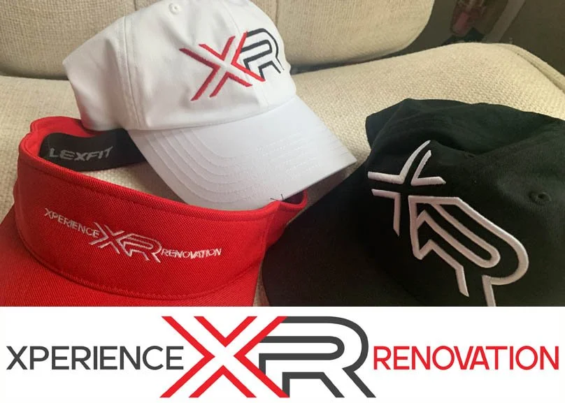 A white baseball cap with XRR logo, a red visored cap with XRR EXPERIENCE RENEWAL text, and a black cap with a white XRR logo, all placed on a beige couch.