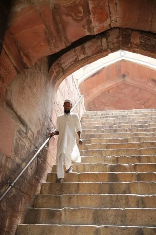 A man dressed in white traditional attire walking down stone stairs inside a historic structure with arched ceilings.