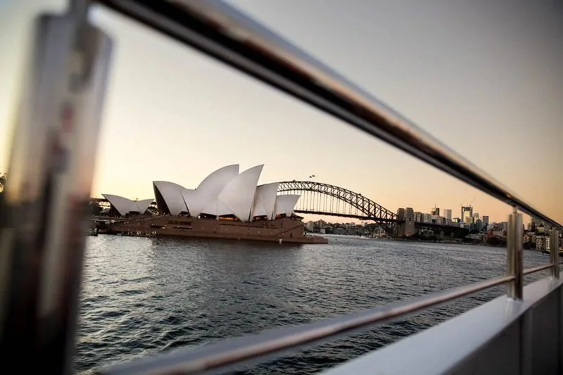 View of the Sydney Opera House and Sydney Harbour Bridge from a boat on the water during sunset.