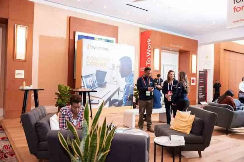 People socializing in a modern conference lounge with sofas, plants, and promotional banners.