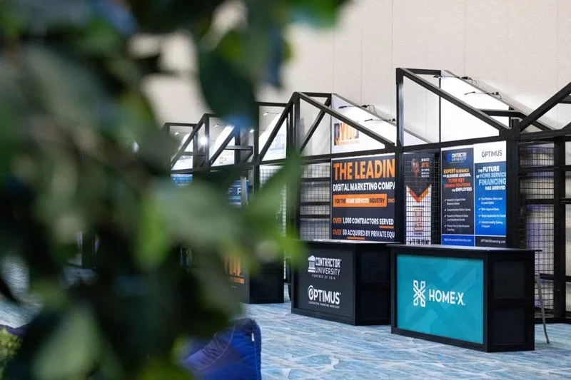 Exhibition booth with banners and screens promoting digital marketing, contractor university, and home X at a conference.