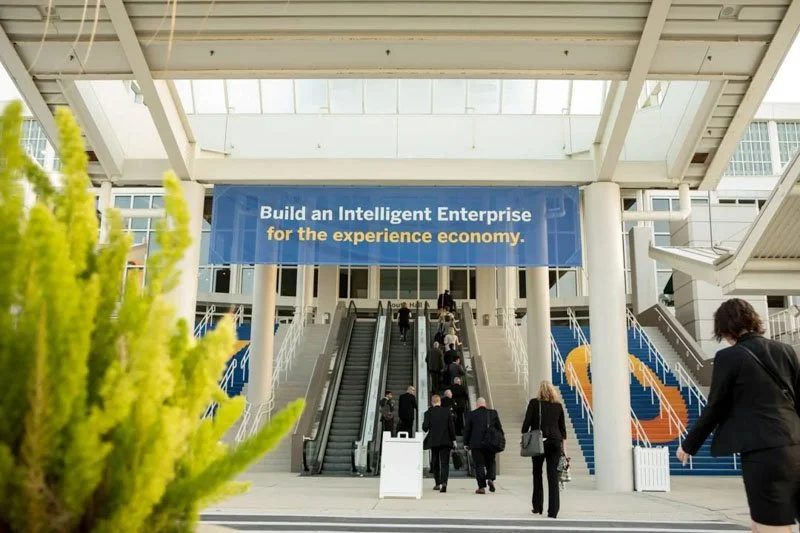 People walking up the escalators at a conference center with a banner that reads "Build an Intelligent Enterprise for the experience economy."