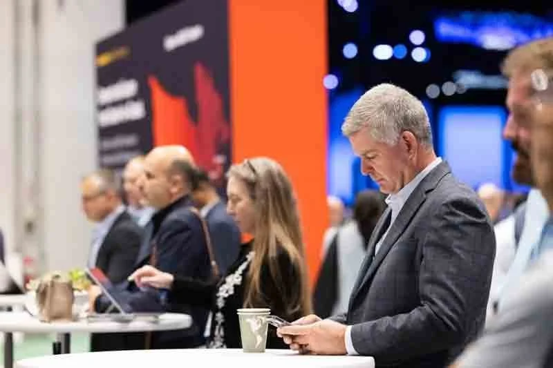 Business professionals at a conference or event, standing at a table using their phones.