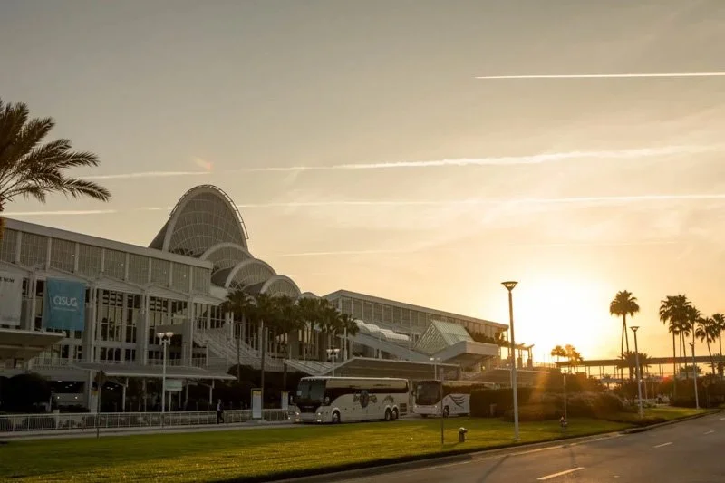 Sunset view of a modern convention center with palm trees and parked buses.