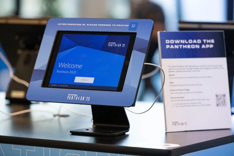Tablets displaying the Pantheon 2023 welcome screen with the text 'Welcome Pantheon 2023' and a sign promoting the Pantheon app download.