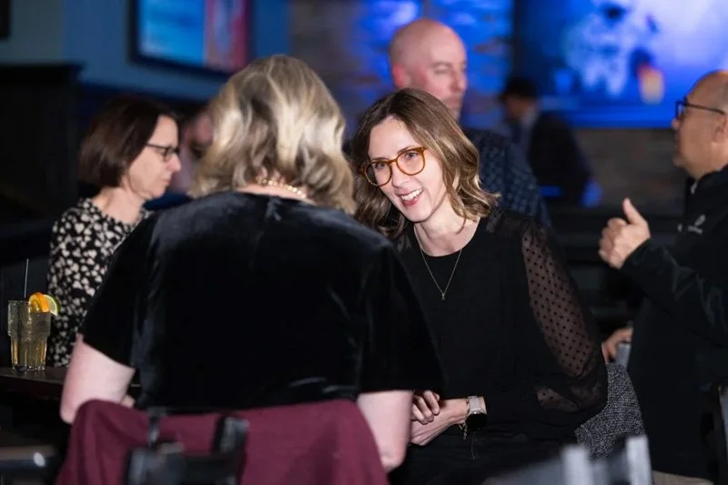 A group of people socializing at a bar or restaurant, with some engaged in conversation.
