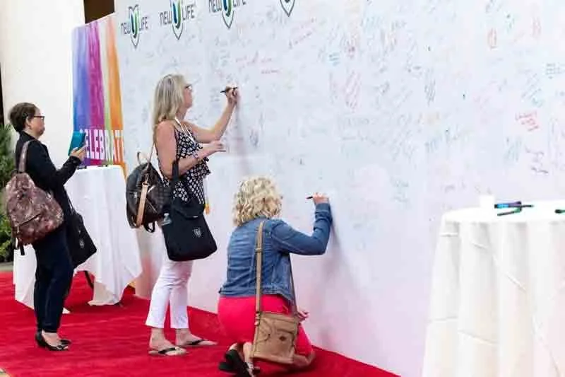 People signing a large white wall, possibly at an event or conference.