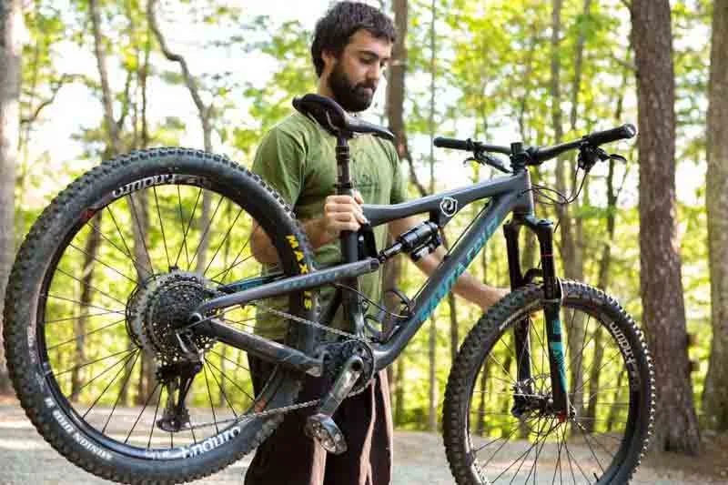 A man holding a mountain bike in a forest setting.