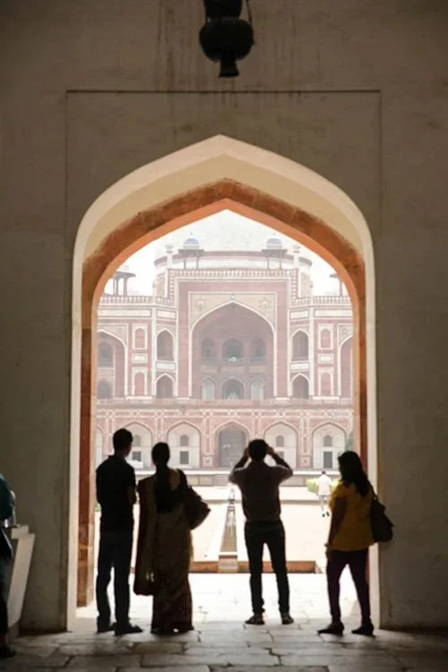 People standing in front of a large archway, looking at a historic building with intricate architecture in India.