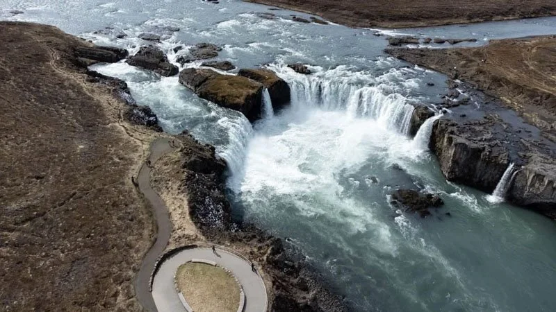 Aerial view of a river with waterfalls and a winding trail or road alongside it.