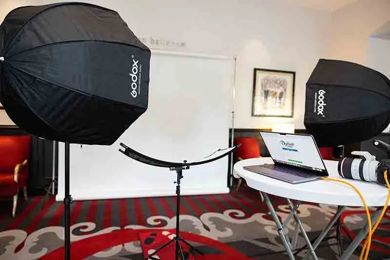 Photography studio setup with two large Godox softbox lights, a laptop on a white table, camera equipment, and a photography backdrop in the background.