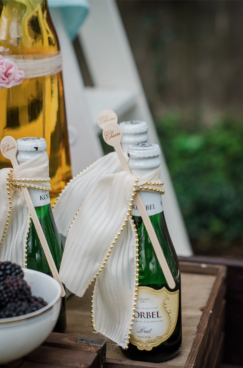  Mini Champagne Bottles presented with fancy ribbon and a cheers drink stirrer attached — Click to see 8 DIY Wedding Ideas for a Springtime Bridal Shower Brunch — Part of the 37 Creative DIY Wedding Ideas for Spring as seen on www.BrendasWeddingBlog.