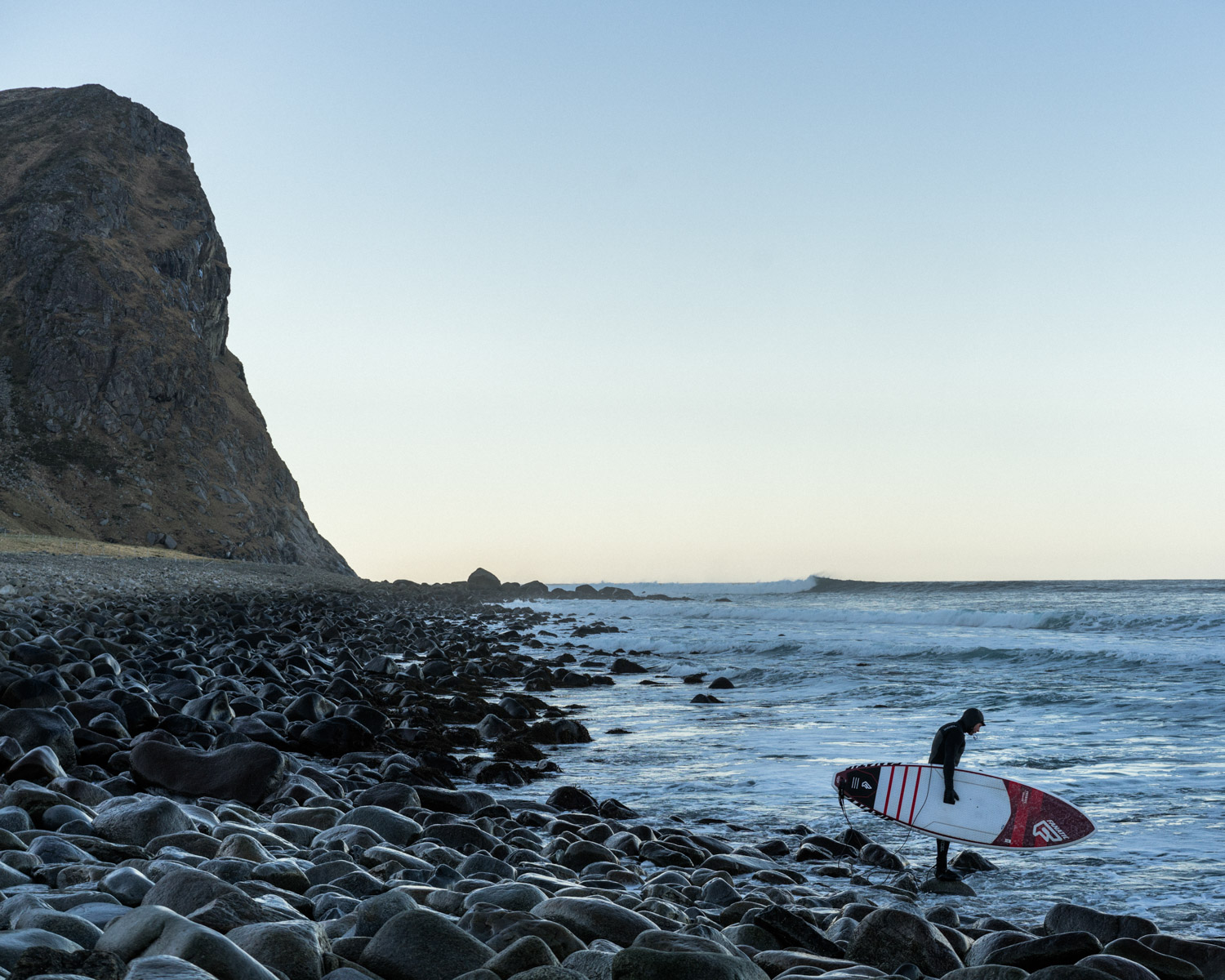 A local surfer getting ready to enter the icy water of the arctic sea in the Lofoten island .