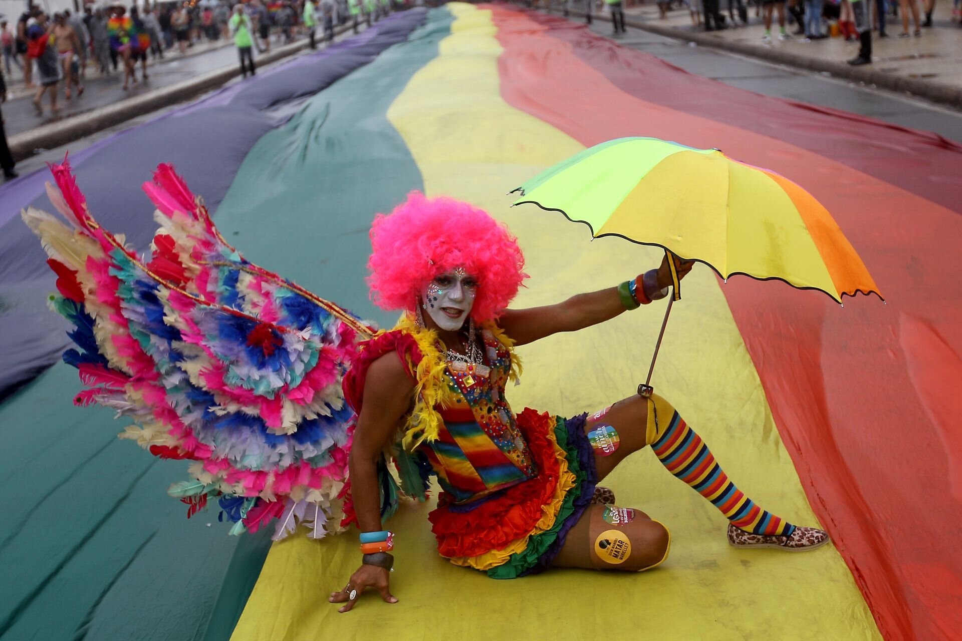 Artista posa para foto sentado na bandeira na 24ª Parada do Orgulho LGBTI  na Praia de Copacabana. 