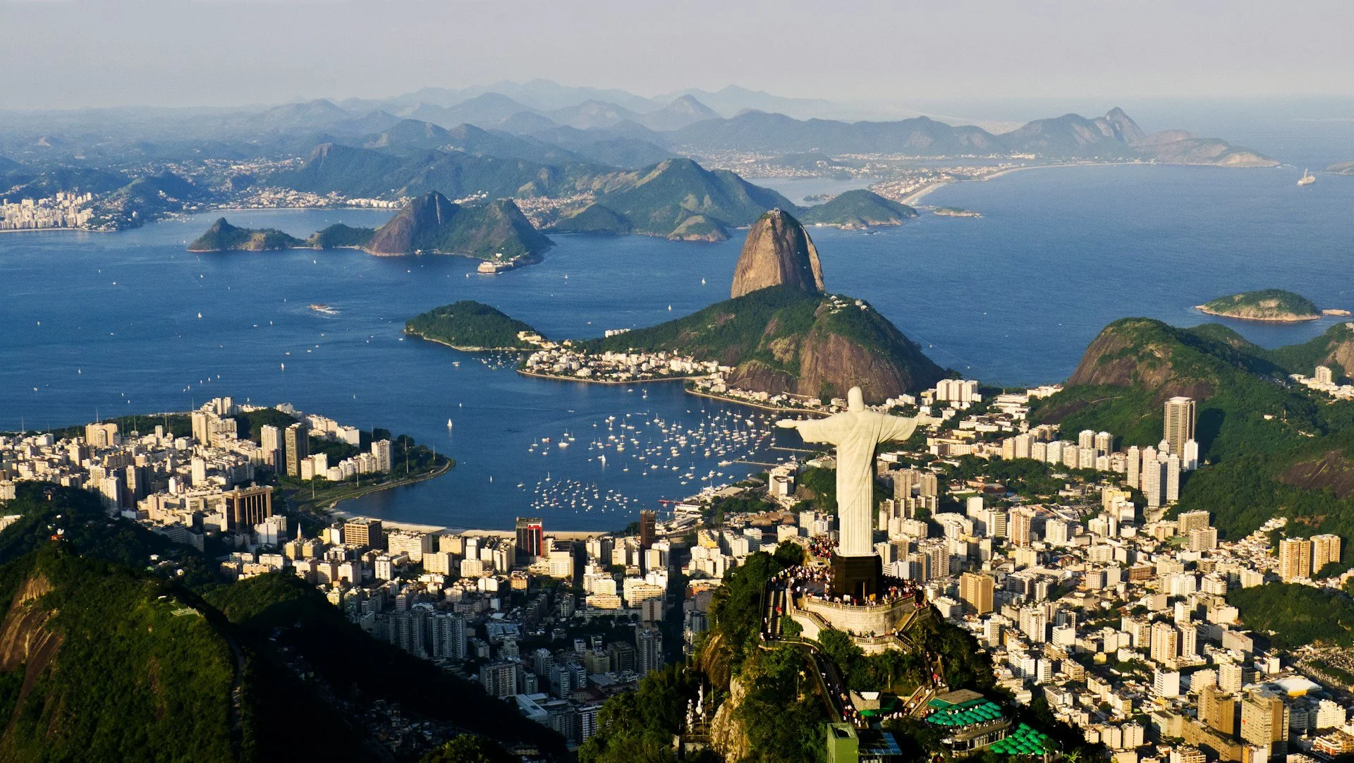 Vista aérea do Rio de Janeiro, com o Cristo Redentor em destaque, o Pão de Açúcar e a Baía de Guanabara ao fundo