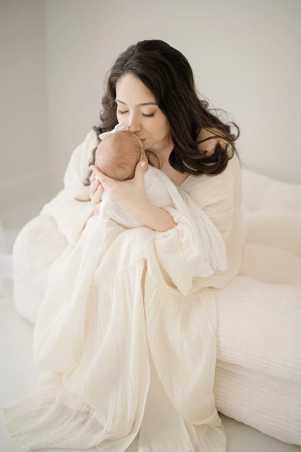 A woman holding and kissing a newborn baby in a softly lit room.