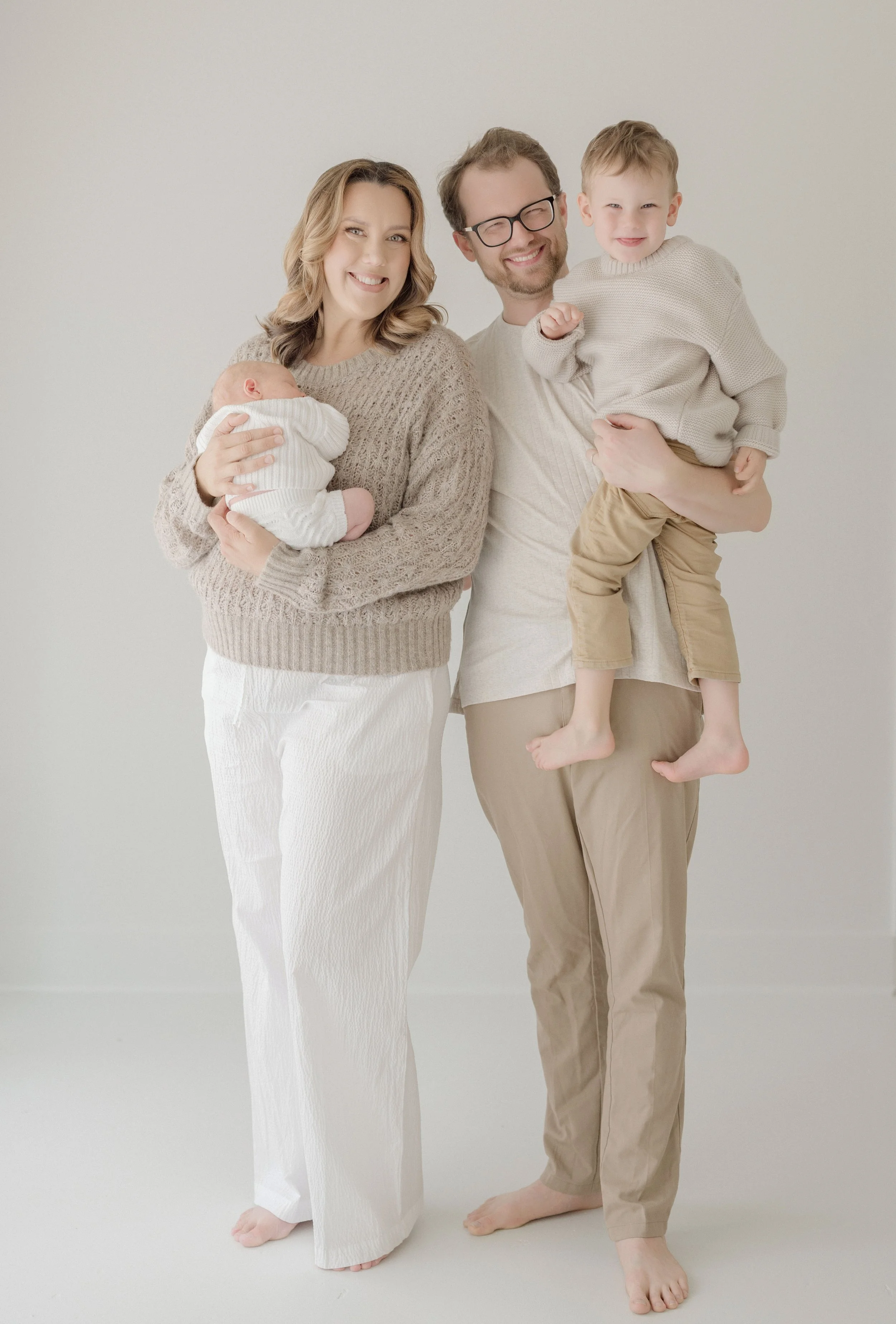A family of four, including a woman, a man, and two children, smiling and posing against a plain white background. Baton Rouge Maternity Newborn and Family Photographer 