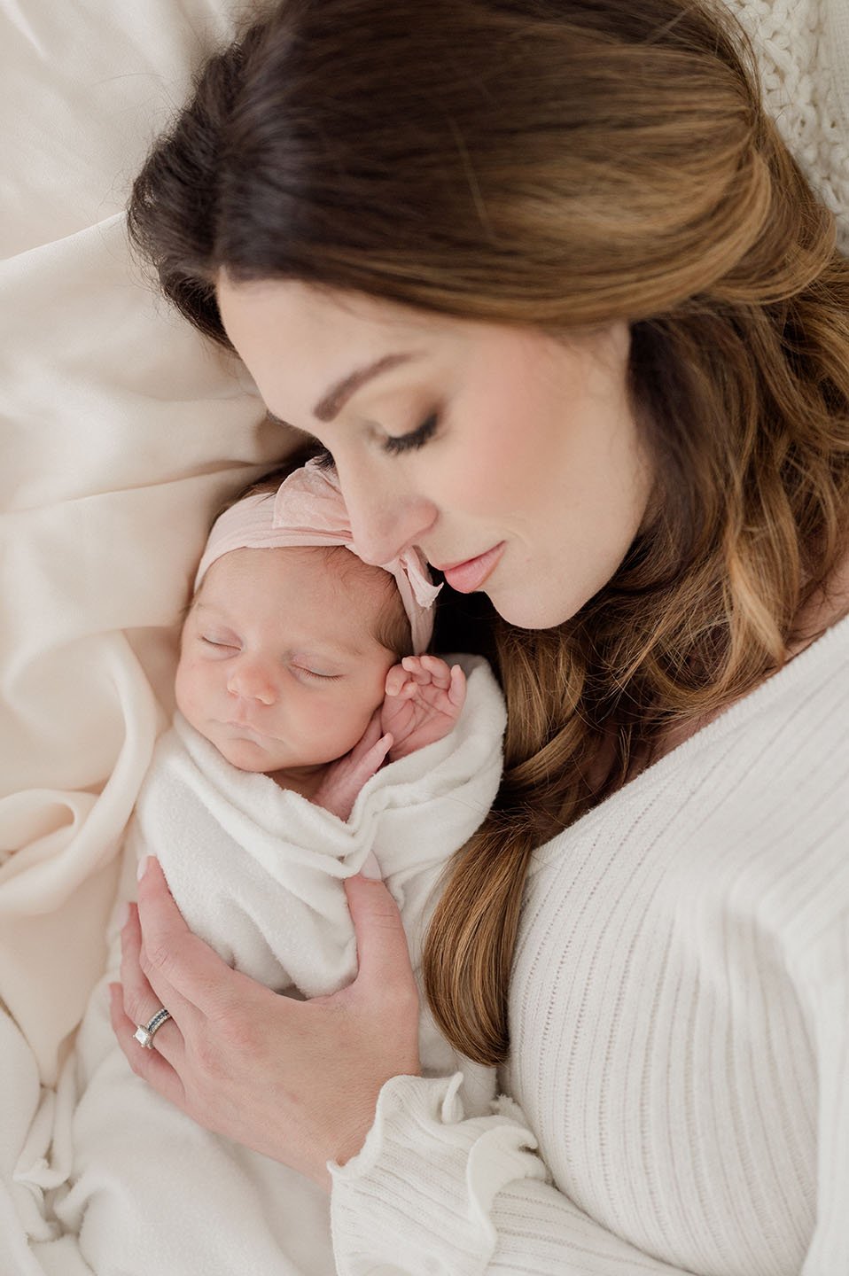 A woman lovingly holding a sleeping newborn baby wrapped in a blanket.