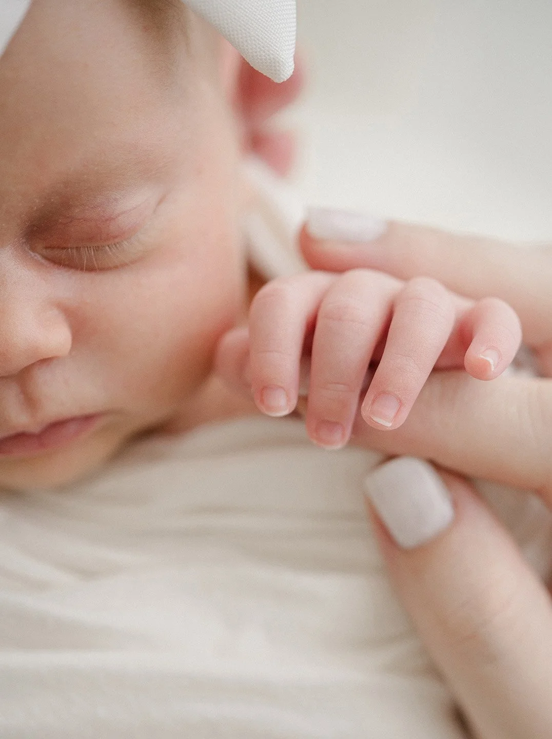 Close-up of a sleeping baby resting their head on a soft surface, with a caregiver gently holding their hand.