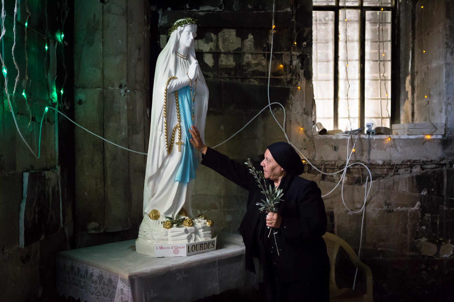  QARAQOSH, IRAQ - MARCH 25, 2018: A woman worshipping a Statue of the Virgin Mary in the burned by ISIS Church of the Immaculate Conception, Al-Tahira church, in Qaraqosh (also known as Hamdaniya) some 30 kilometers from Mosul. Christians of Qaraqosh