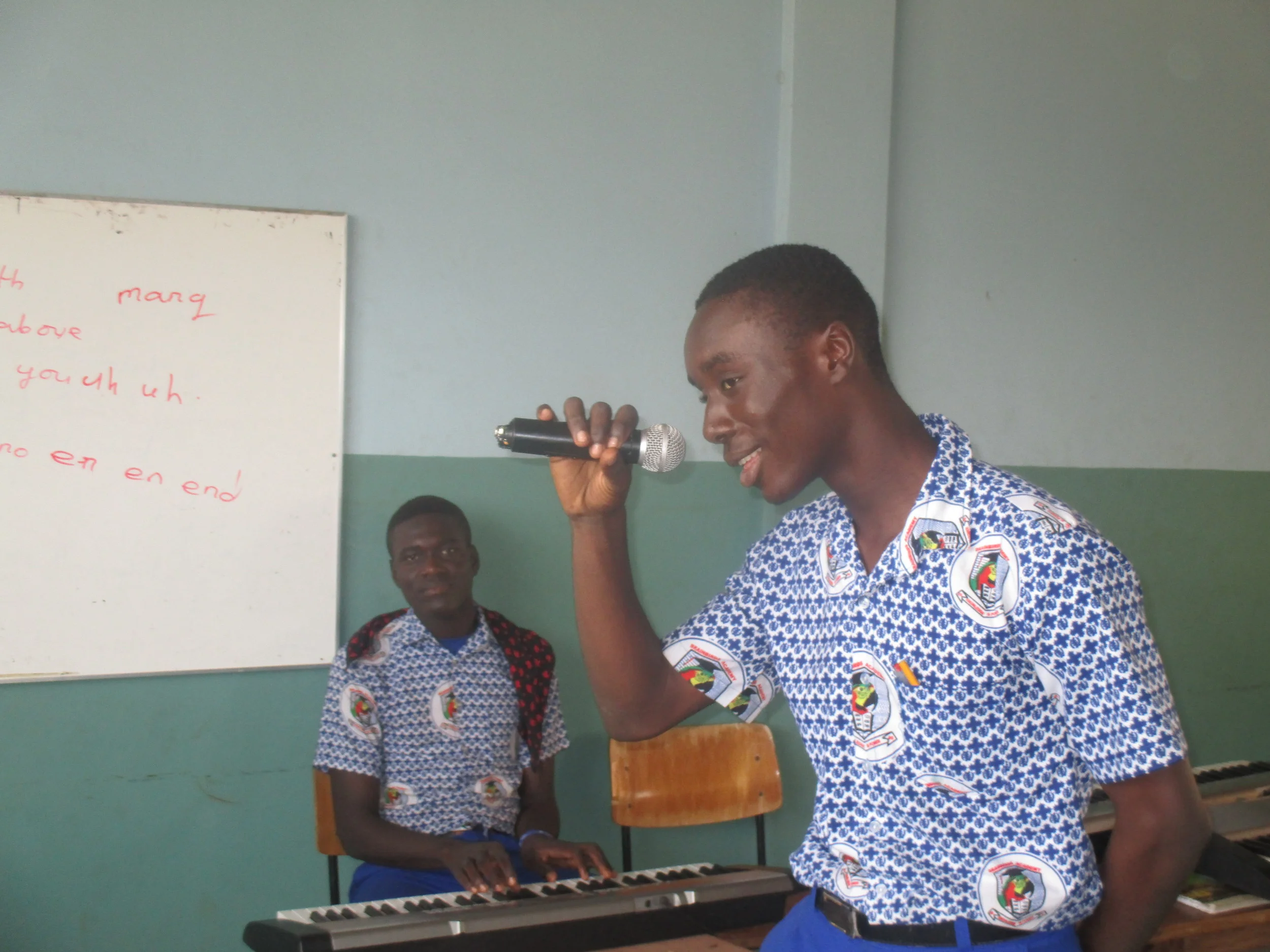 A photograph of Josh singing (and other Josh playing the keyboard) at graduation rehearsal, by Osman, Class 6.