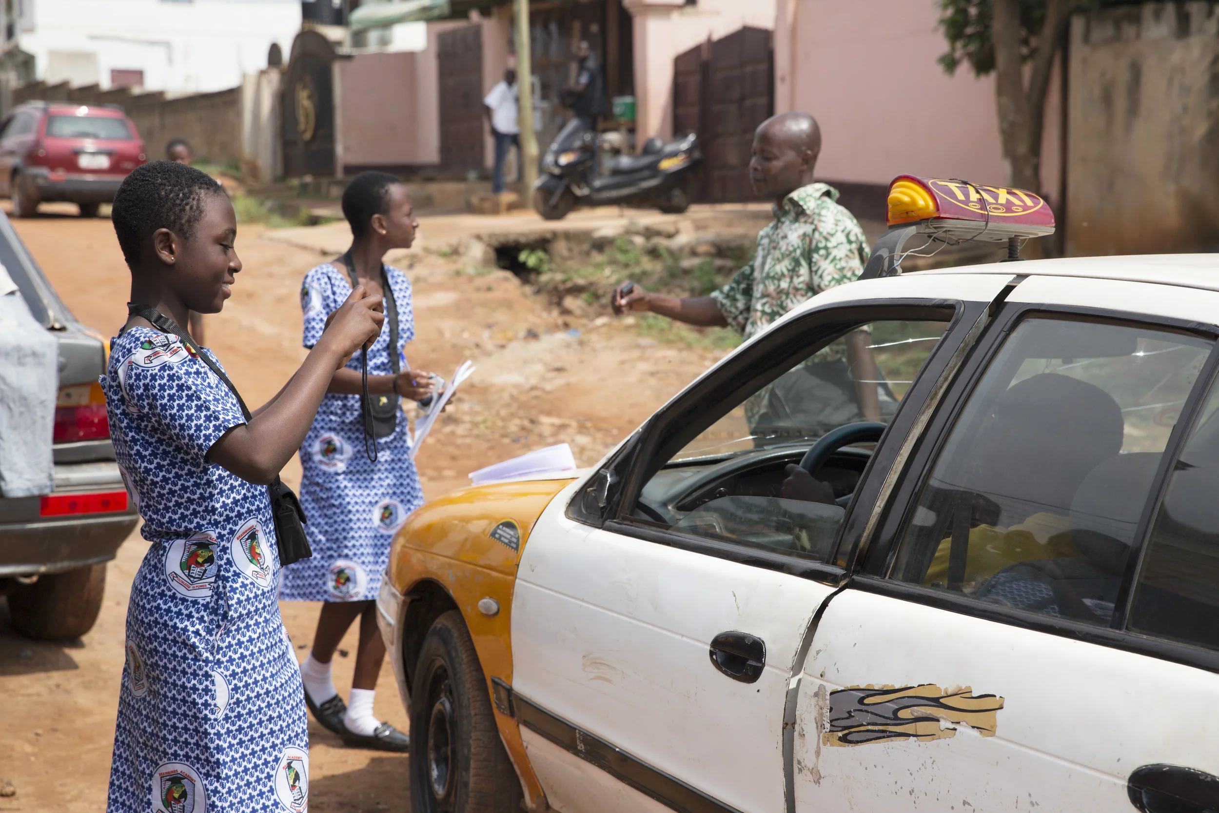 Hectoria interviews someone, while Constance photographs a taxi driver.