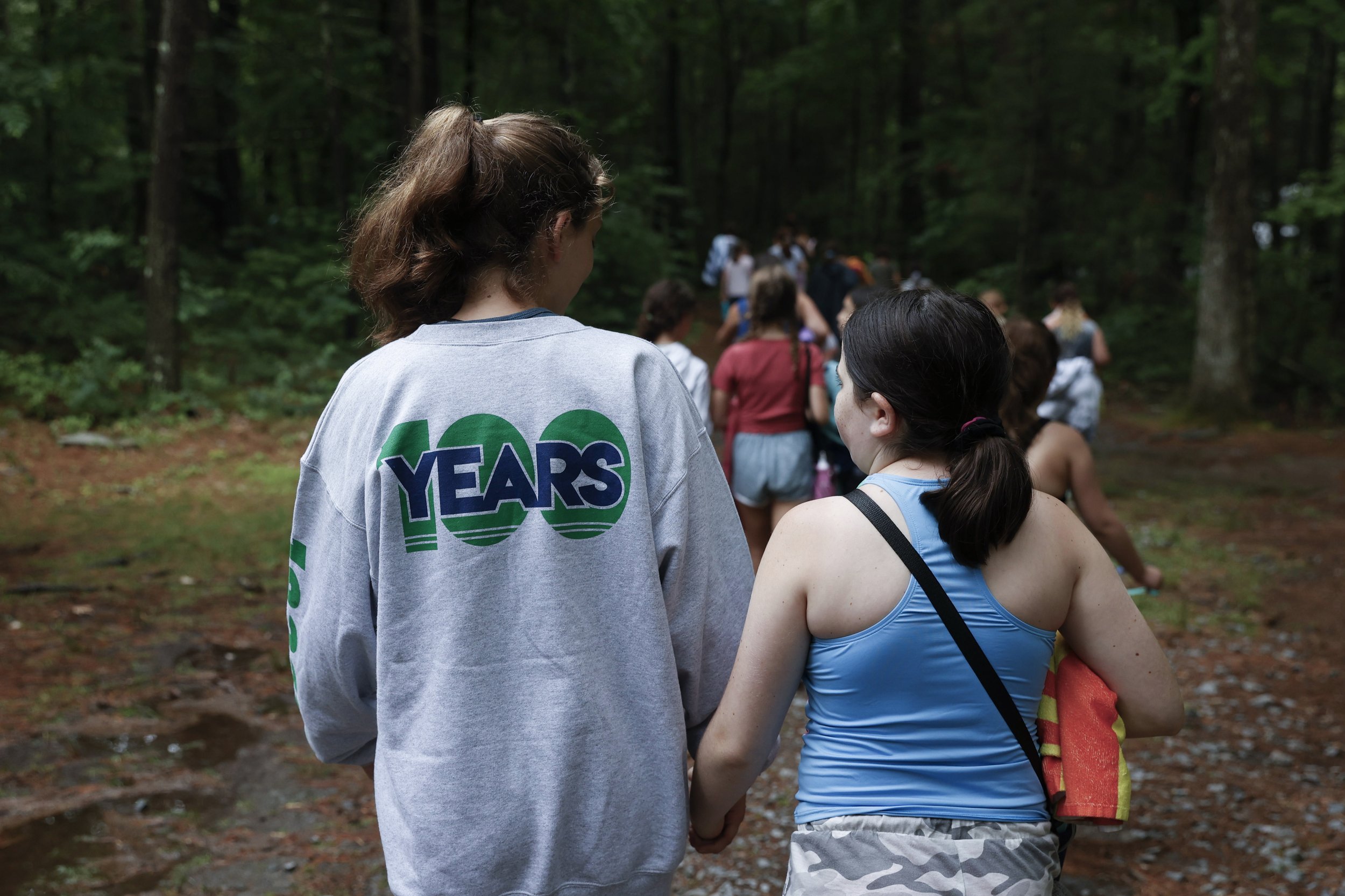  Eli Gross (left), the head counselor of Bunk 37 (and a former Nah-Jee-Wah camper), walks arm in arm with Amelia Goldin on the bunk’s way to canteen on July 8, 2021. Eli’s shirt has a graphic to represent that this year is the “100th summer” of Nah-J