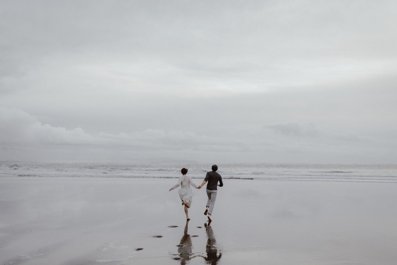 A couple runs on the sand at their Oregon coast engagement session