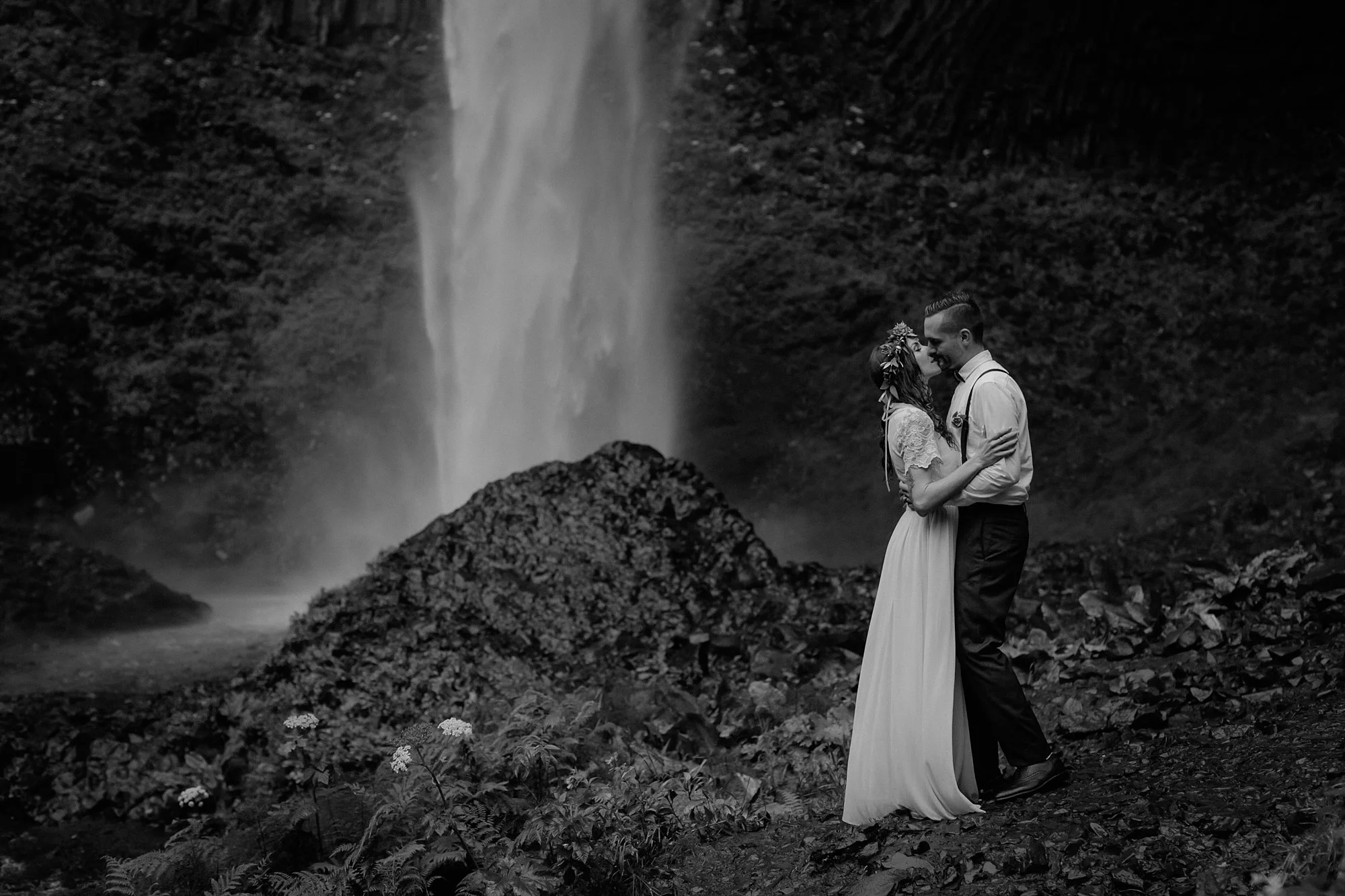 The bride and groom kiss in front of a waterfall.