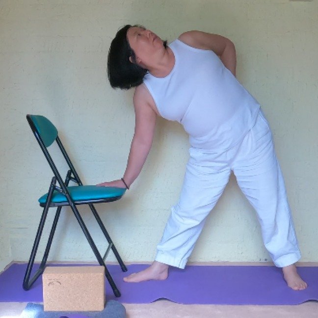 Debbie performing a side bend with her hand resting on a chair for support