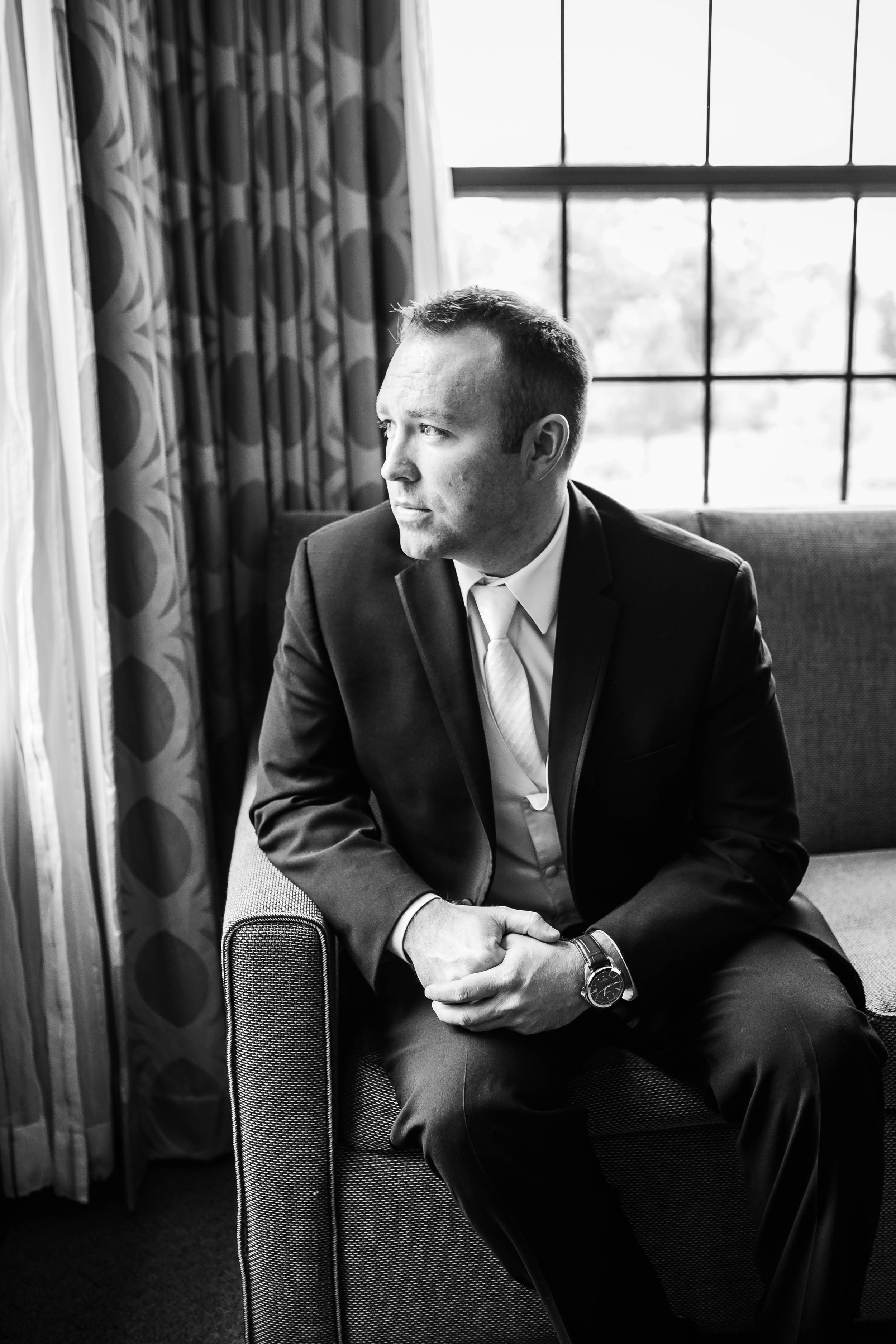 black and white portrait of groom looking out a window