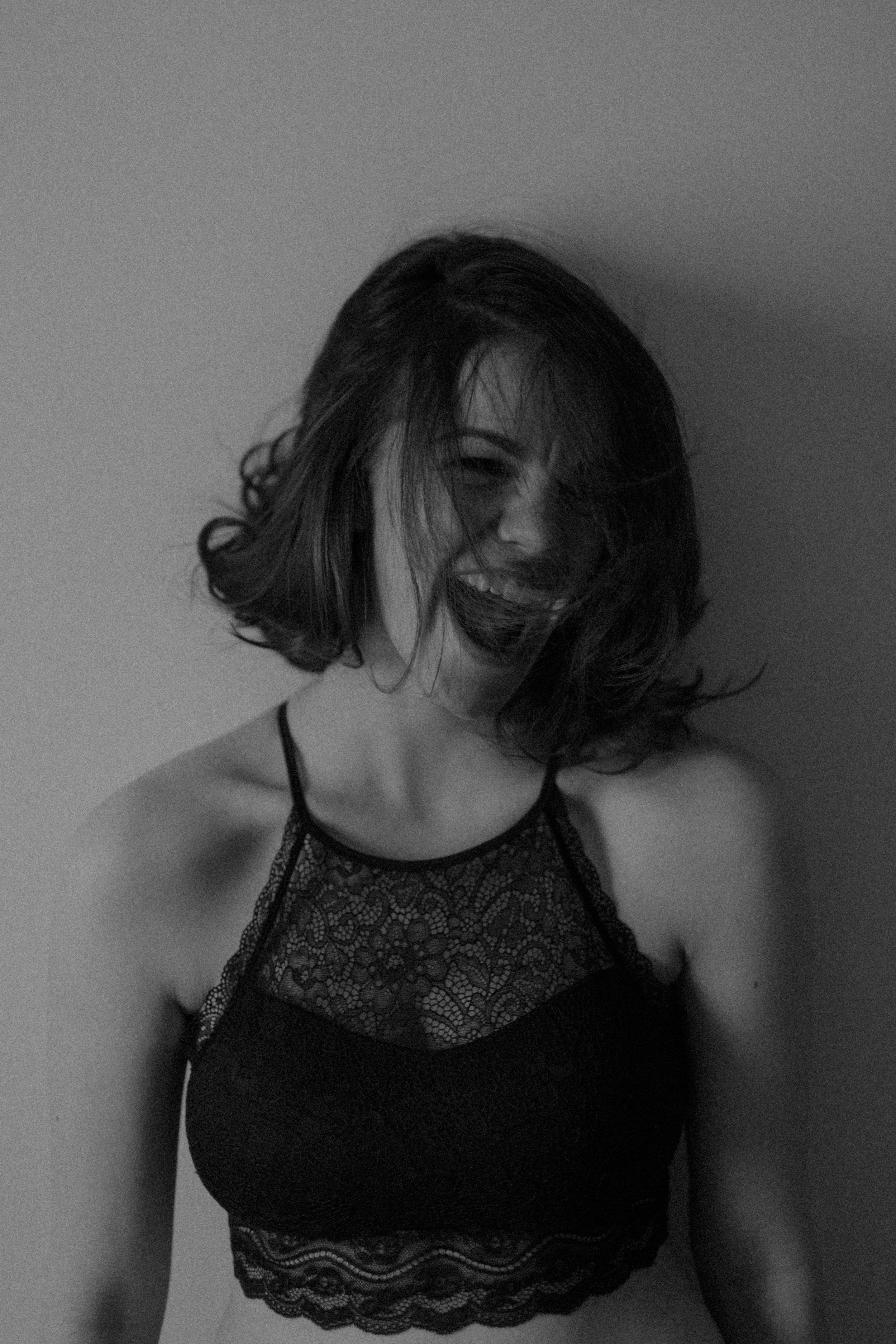  a black-and-white portrait of emma grimsley in a victorian airbnb in dayton, ohio. emma is laughing as her hair covers her face and she is clothed in a black lace crop top bralette. photograph by sarah rose walk of sarah rose photography. 