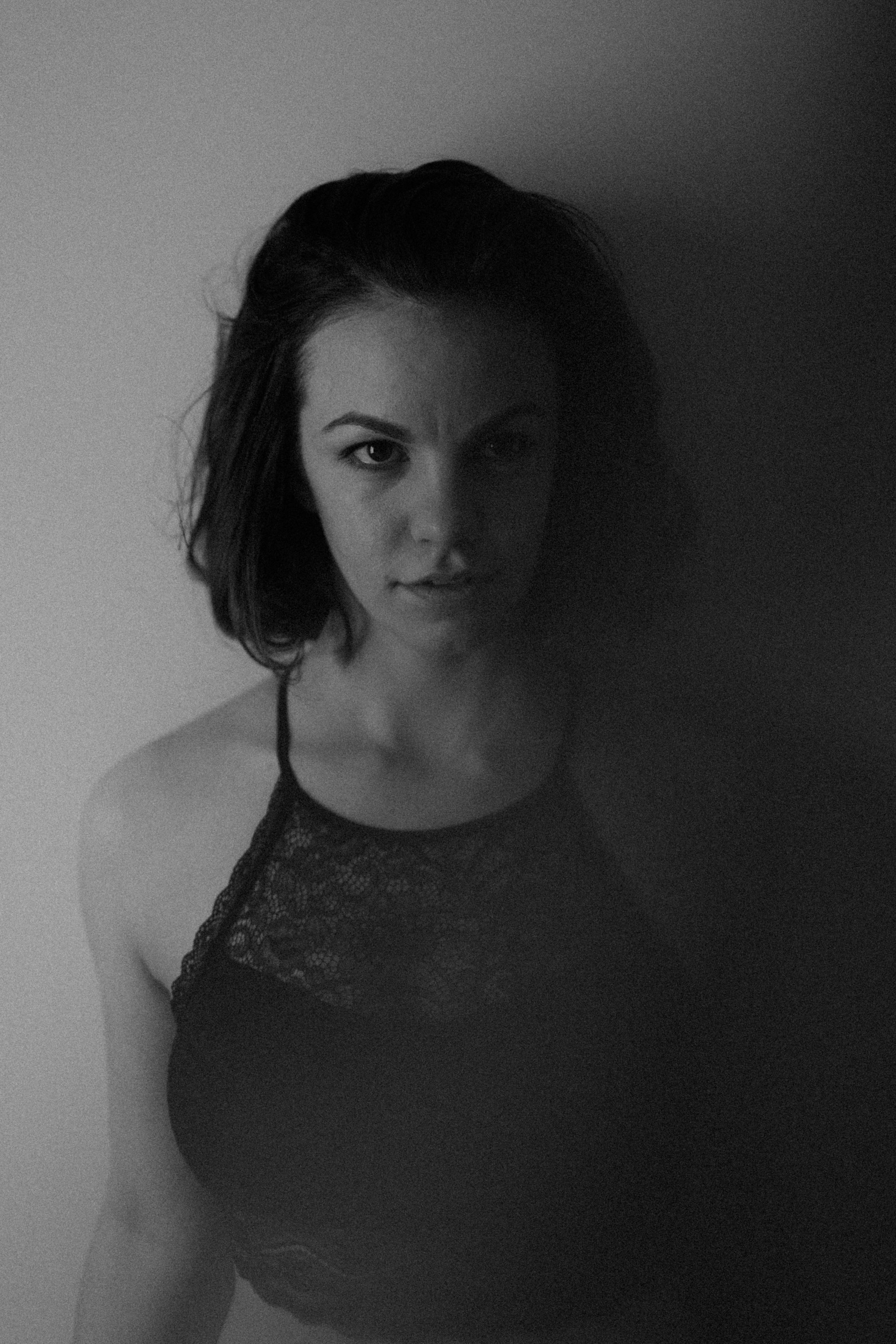  a black-and-white portrait of emma grimsley in a victorian airbnb in dayton, ohio. a piece of fabric is floating through the air, covering part of her torso. emma is clothed in a black lace crop top bralette. photograph by sarah rose walk of sarah r