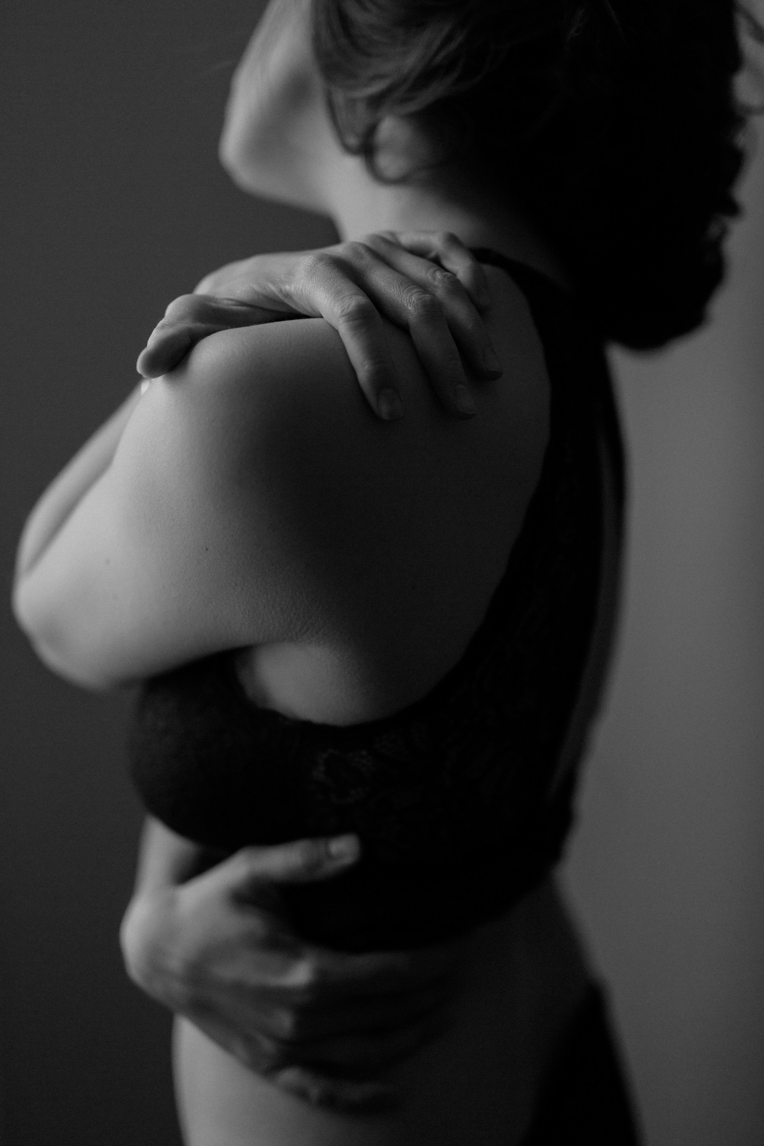  a black-and-white portrait of emma grimsley in a victorian airbnb in dayton, ohio. the photograph is of her torso from behind, and the focus is on her hands as she wraps one around her waist and one on her shoulder. photography by sarah rose walk of